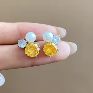 Detailed close-up of dainty silver stud earrings featuring yellow zircon flower and pearl.