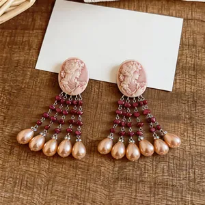 Close-up view of vintage cameo dangle earrings with burgundy beads and pearl tassels decor