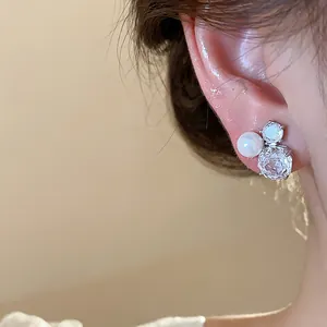 Detailed macro view of an elegant zircon flower and pearl stud earring worn on the ear.