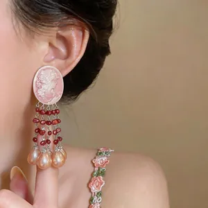 Detailed shot of pink cameo earrings with teardrop pearls and red beaded tassels
