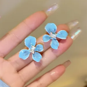 Macro detail showing light blue flower-shaped stud earrings with a sparkling center crystal stone
