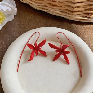 Detalle de pendientes con forma de flor roja y ganchos largos curvados de diseño moderno