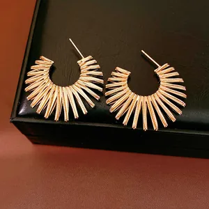 Detailed macro view of gold sunburst C-shaped earrings on a black jewelry box