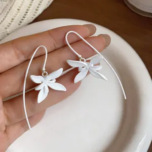 Detalle de pendientes de flores blancas mate con elegantes ganchos largos y curvados