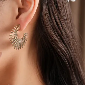 Close-up view of elegant gold C-shaped earrings with a sunburst radiating texture