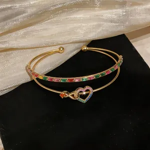 Macro detail of gold-plated bangle featuring heart and infinity motif with multi-colored zircons