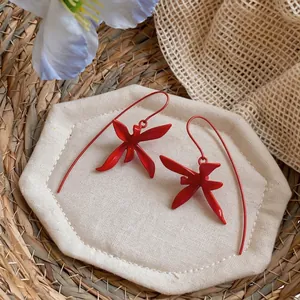 Detalle de pendientes de orquídea roja mate con ganchos largos y curvados.