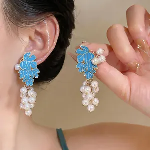 Close-up detail of grape cluster earrings featuring blue enamel leaves and white pearls.