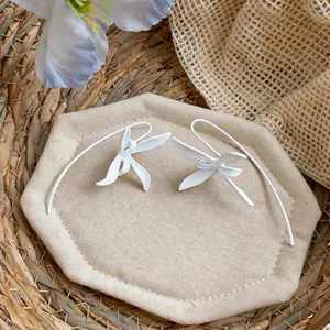 Primer plano de pendientes de gancho con flores blancas mate de diseño minimalista.
