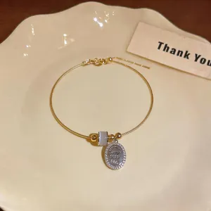 Detail of gold-colored bracelet featuring a cat's eye stone and shimmering oval charm