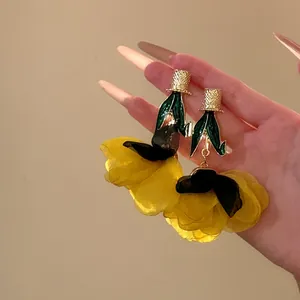 Détail de boucles d'oreilles fleurs en tissu jaune avec feuille verte et clou doré