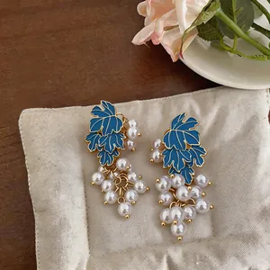 Close-up of elegant grape-shaped earrings with blue enamel leaves and white pearls
