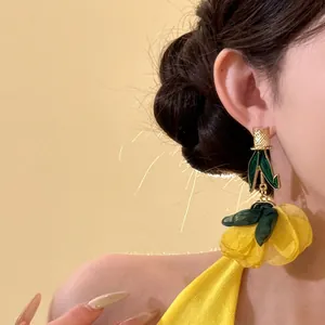 Vue macro détaillée de boucles d'oreilles fleurs jaunes surdimensionnées en tissu et or