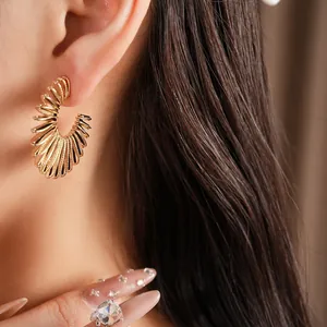 Close-up view of a gold C-shaped earring with spiral texture worn on the ear