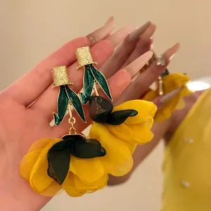 Vue détaillée de boucles d'oreilles fleurs jaunes en tissu avec accents de feuilles