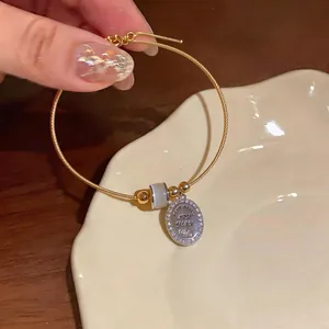 Close-up of zircon-encrusted oval charm and cat's eye bead on a gold wire bangle