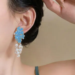 Close-up detail of blue enamel leaf and pearl grape cluster earrings on model's ear