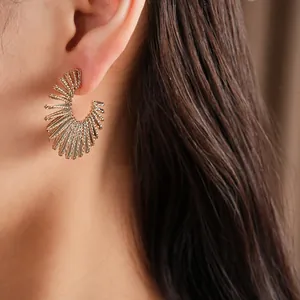 Close-up of a gold sunburst C-shaped earring on ear, showing metallic texture