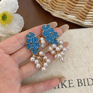 Close-up detail of grape-shaped drop earrings with blue enamel leaves and white pearls