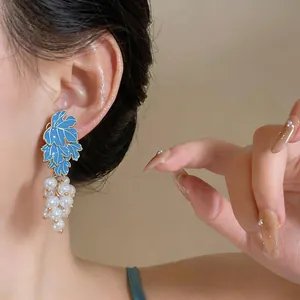Close-up view of elegant blue enamel leaf and white cluster pearl grape earrings on model