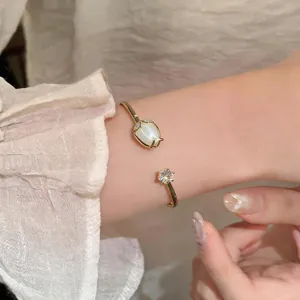 Detail of a gold open bangle featuring a white cat's eye tulip and a sparkling zircon.