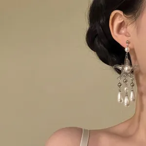 Detailed view of ornate silver starfish tassel earrings with white pearls on a model
