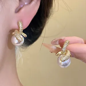 Dettaglio di orecchini placcati oro 18K con zirconi scintillanti e perle bianche.