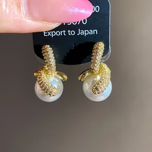 Dettaglio di eleganti orecchini pendenti con perle e zirconi placcati in oro 18K