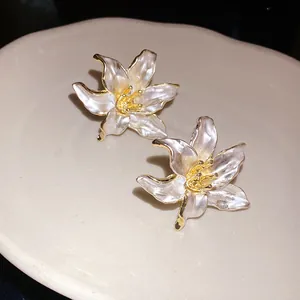 Detailed view of vintage white enamel flower earrings with gold edges on a ceramic tray.