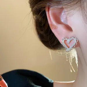 Close-up detail of a silver heart-shaped earring with zircons on a model's ear