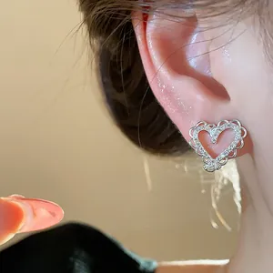 Close-up detail of elegant silver heart earring with shiny zircon inlay on model's ear
