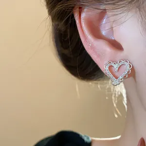 Close-up view of heart-shaped silver earrings with sparkling zircons on a model's ear.