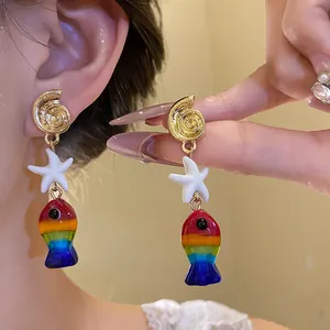Dettaglio ravvicinato di orecchini a forma di pesce arcobaleno e stella marina con conchiglia.