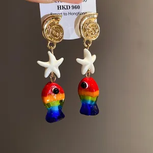 Dettaglio di orecchini a tema marino con pesci in vetro arcobaleno e stelle marine