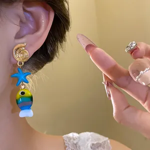 Dettaglio di orecchini a tema marino con pendenti a forma di stella e pesce colorato.