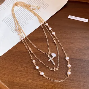 Detailed view of layered gold necklace featuring pearl beads and a crystal cross pendant