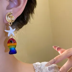 Vista dettagliata di un orecchino a pesce arcobaleno con stella marina e conchiglia su modella.