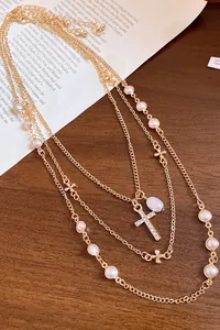 Close-up detail of layered gold necklace with pearls and rhinestone cross pendant.