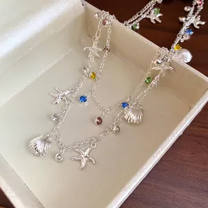 Gros plan d'un collier argenté double épaisseur avec breloques étoile de mer et coquillages.