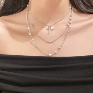 Detail of triple layered necklace with pearls and rhinestone cross pendant on model.