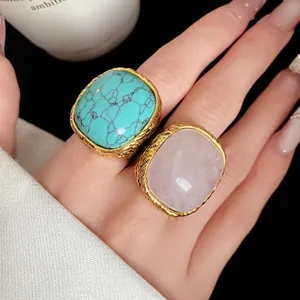 Chunky vintage gold rings with square turquoise and pink crystal stones on hand.