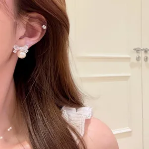 Dettaglio di un orecchino a fiocco in zircone con perla indossato da una modella