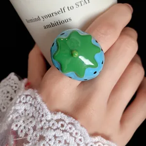 Detailed macro shot of a playful blue strawberry-shaped glossy resin ring worn on a finger