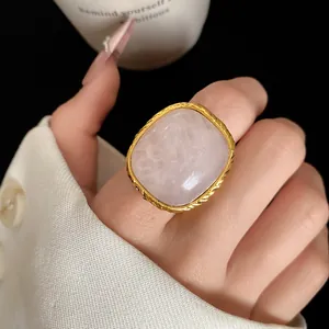 Close-up of retro square pink crystal ring with textured gold frame on finger.