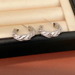 Close-up of silver-plated C-shaped hoop earrings with sparkling zircon stones in a box.