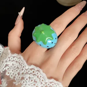 Close-up of a unique blue strawberry-shaped resin ring with green top detail on a finger