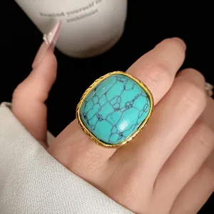 Close-up of vintage square turquoise stone ring with gold textured frame on finger
