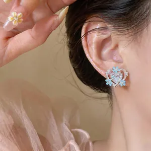 Close-up detail of silver heart stud earrings with blue enamel flowers and crystal center.