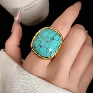 Detailed view of a vintage square turquoise ring with a gold-plated frame on a hand.