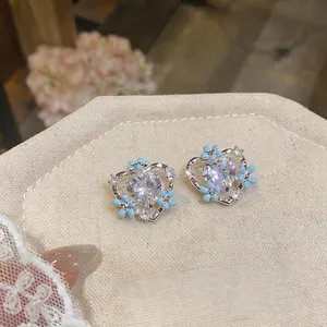 Close-up of heart-shaped silver stud earrings with blue flowers and clear crystals